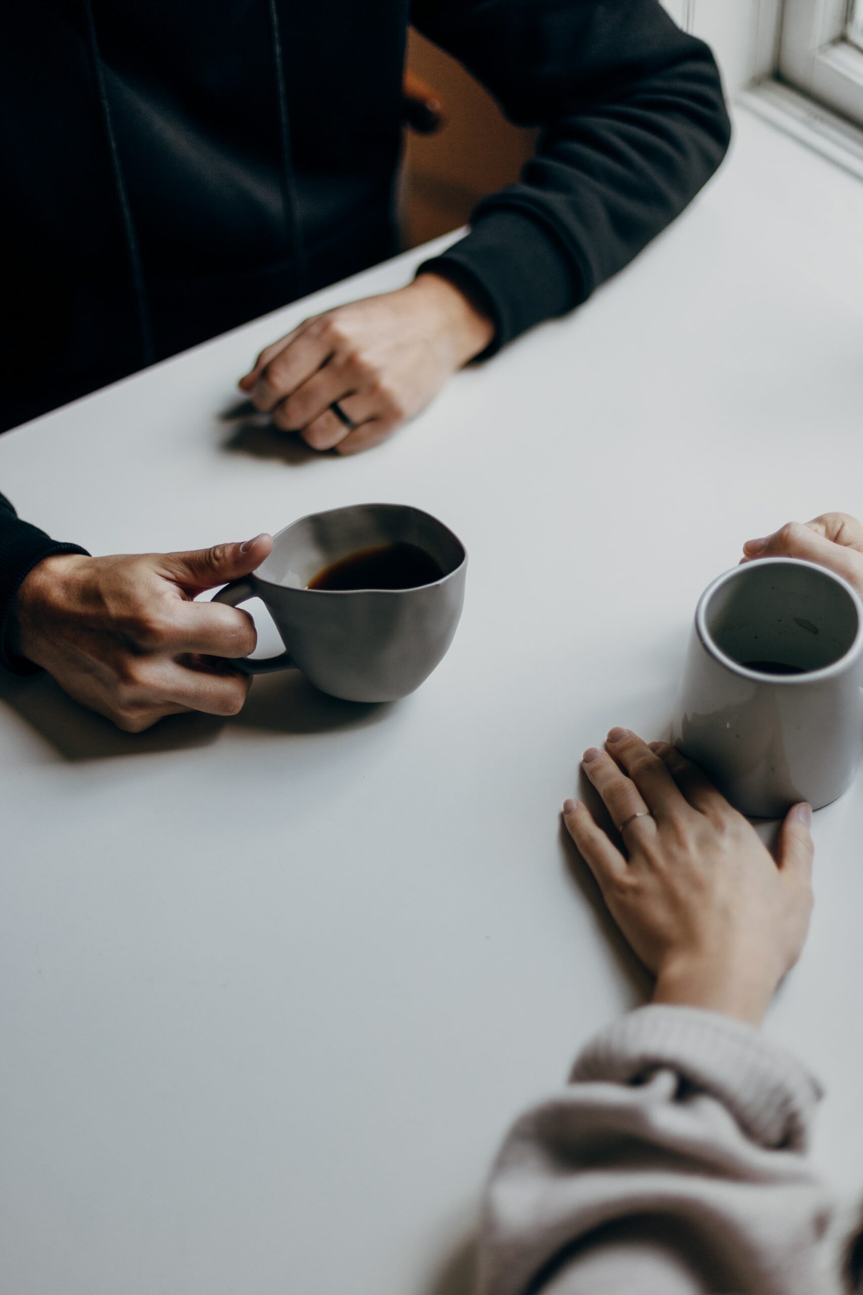 A parent and a support co-ordinator holding coffee mugs at a table.